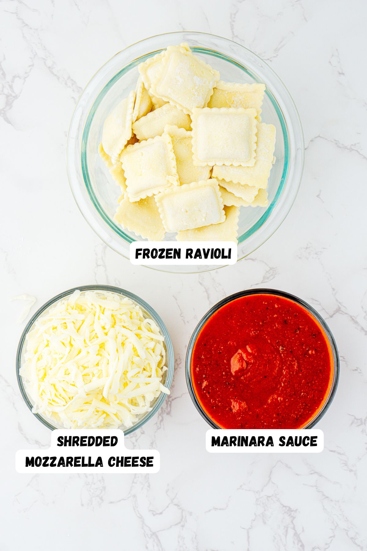 Ingredients needed to make ravioli lasagna measured in clear glass bowls on a white marble table. 