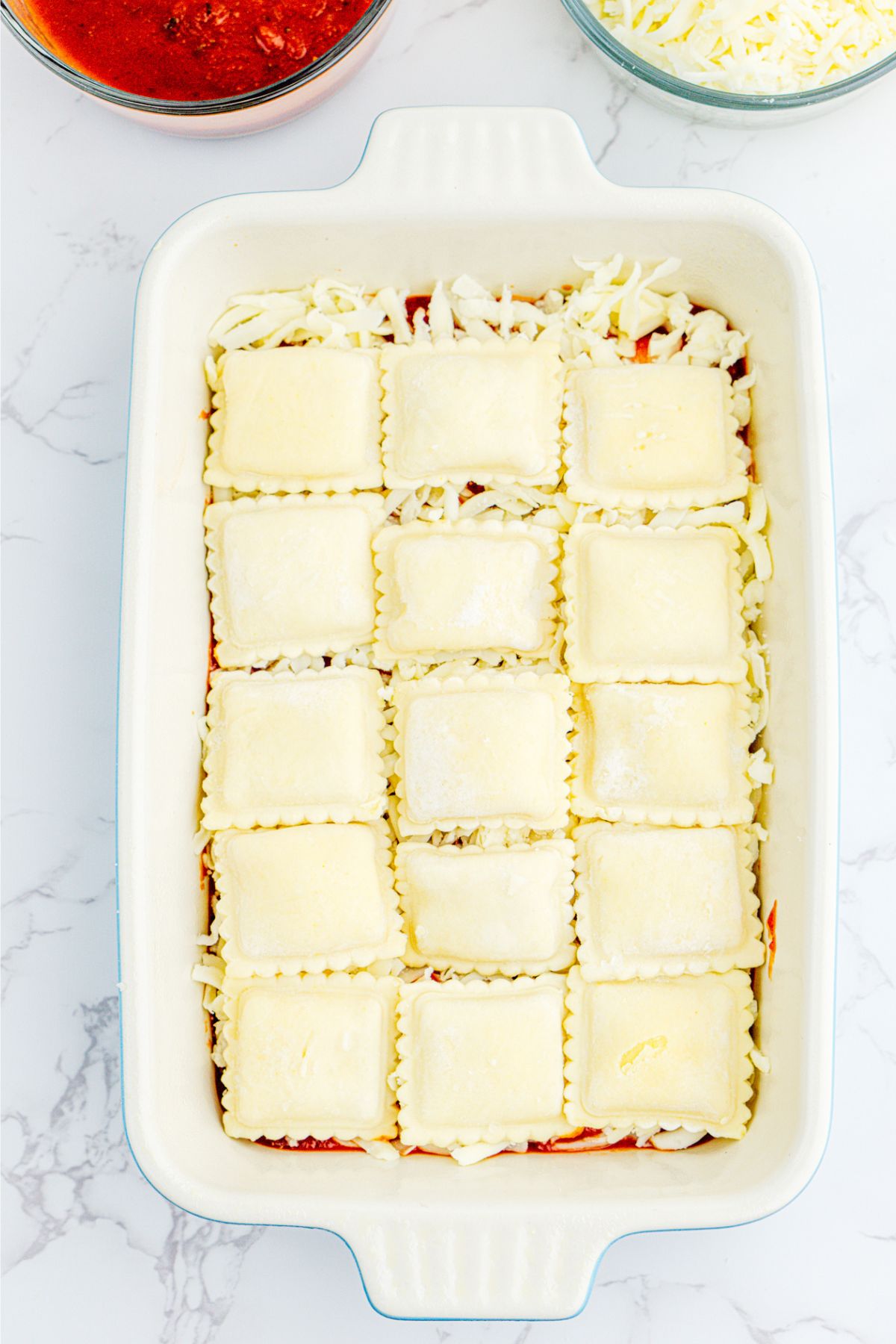 White rectangle dish filled with layers of sauce, ravioli, and shredded mozzarella cheese. 