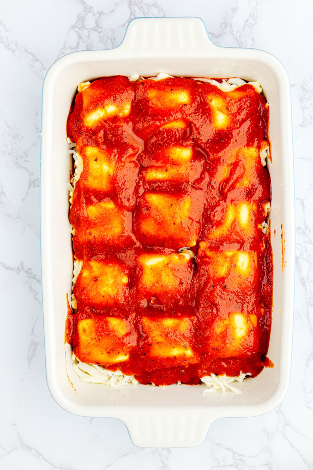 Layers of ravioli, sauce, and cheese, in a white rectangle dish. 