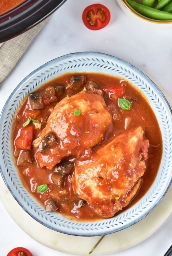 Cooked chicken in a red sauce, with seasonings, in a white bowl.