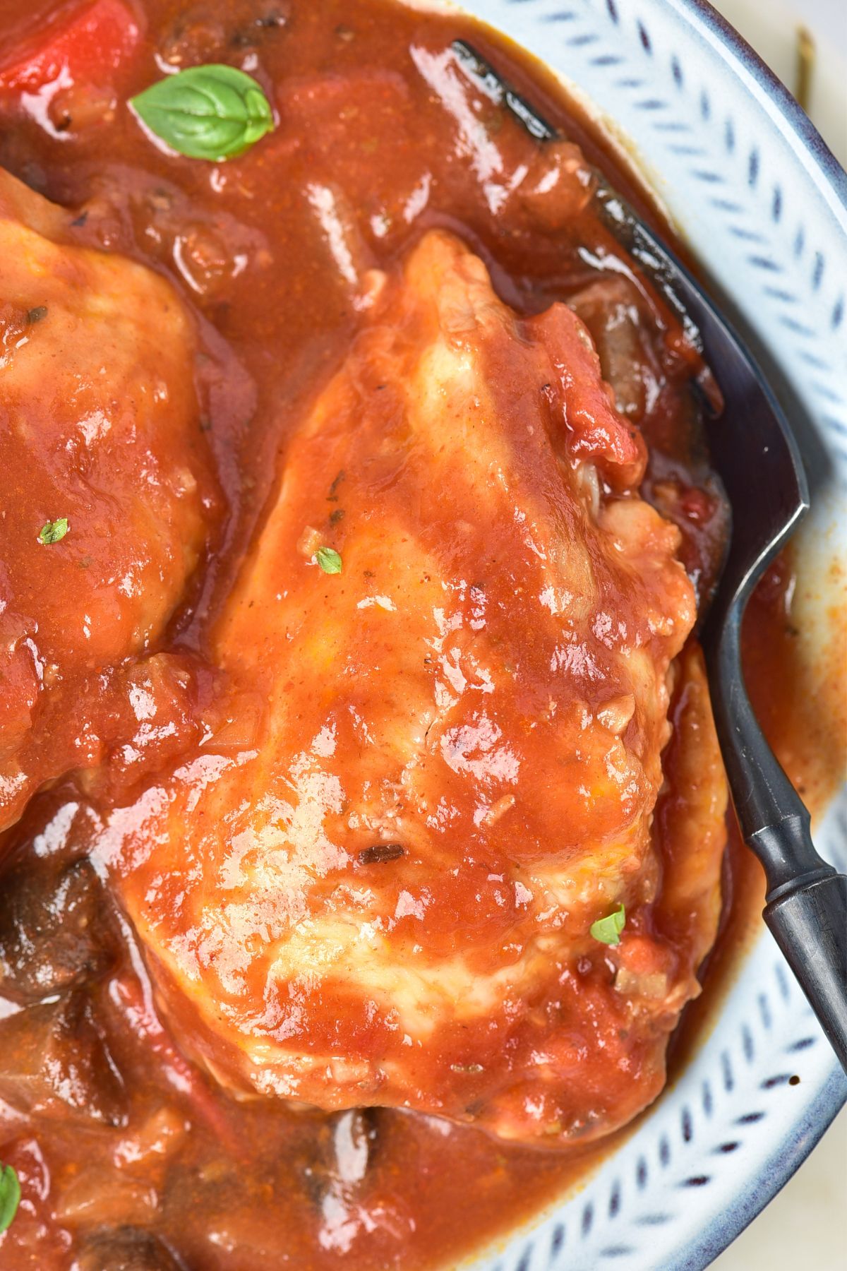 Cooked chicken cacciatore in a red tomato based sauce, with seasonings, in a white bowl. 