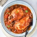 Cooked chicken in a red sauce, with seasonings, in a white bowl.