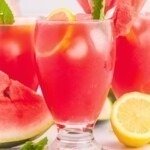 Glasses filled with ice cubes and a pink lemonade, topped with a watermelon slice and pink striped straws.