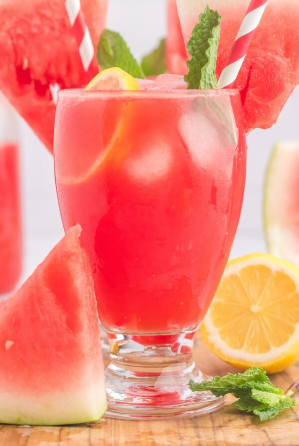 Glasses filled with ice cubes and a pink lemonade, topped with a watermelon slice and pink striped straws.