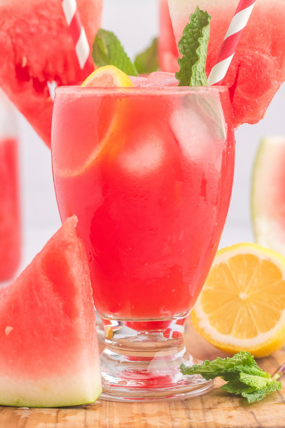 Glasses filled with ice cubes and a pink lemonade, topped with a watermelon slice and pink striped straws.