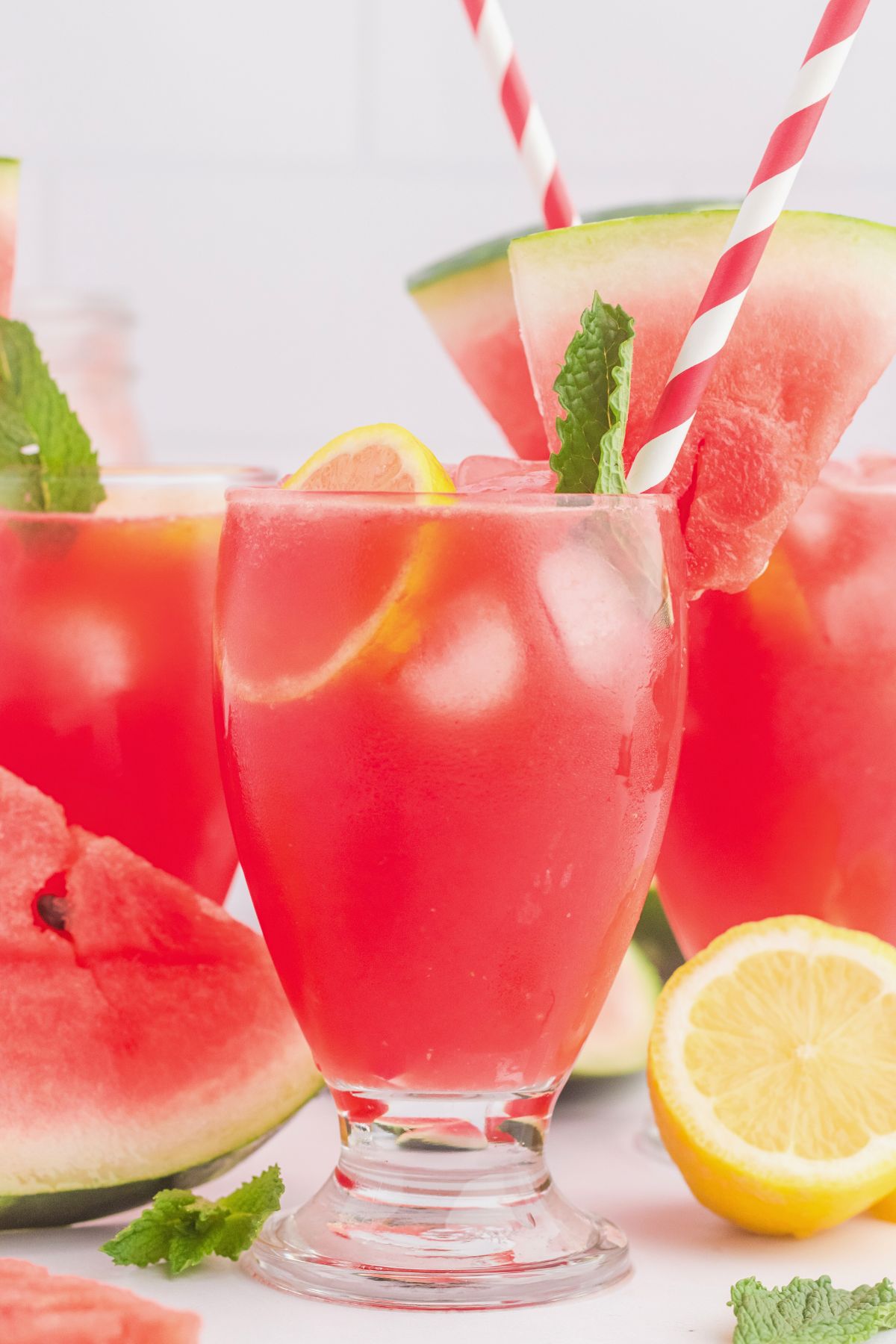 Glasses filled with ice cubes and a pink lemonade, topped with a watermelon slice and pink striped straws.