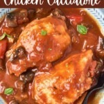 Cooked chicken in a red sauce, with seasonings, in a white bowl.