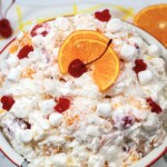 White bowl with fruit salad, topped with cherries and orange slices.