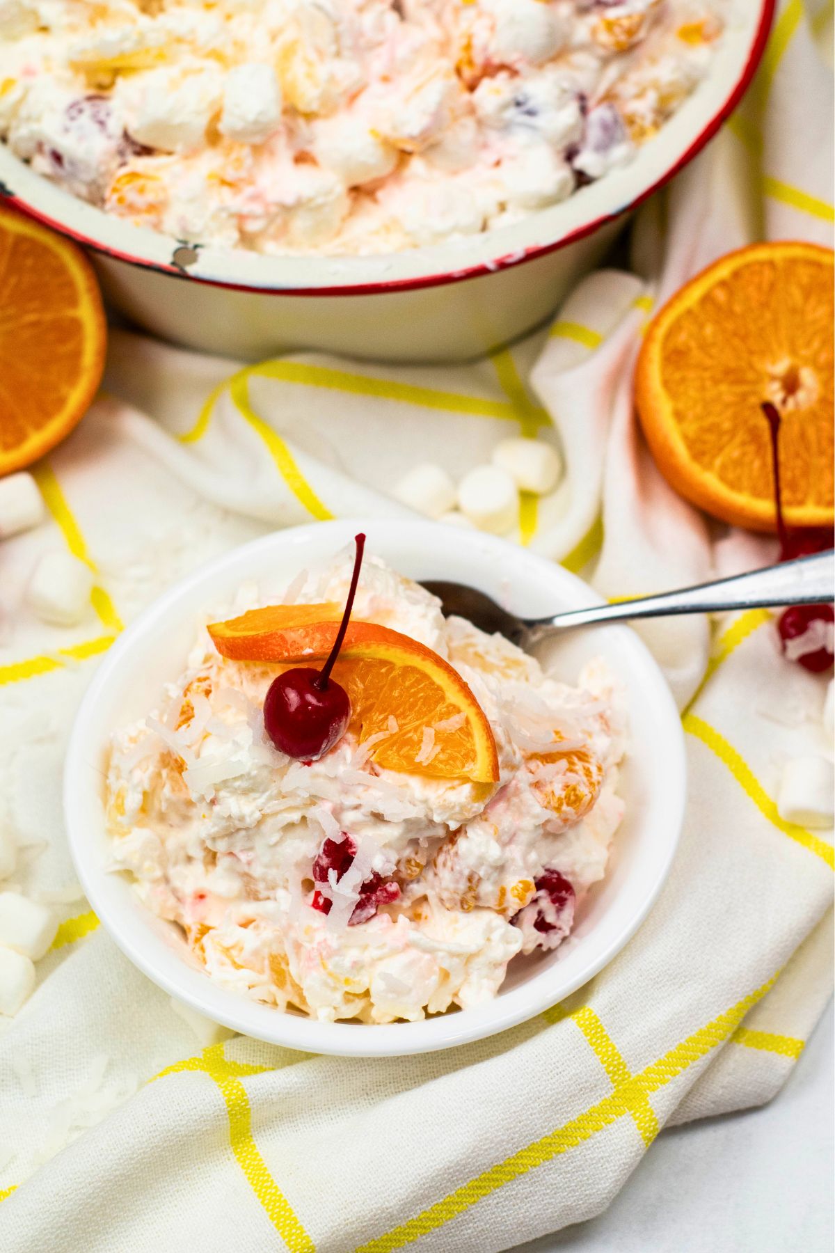Small white bowl with ambrosia fruit salad in the bowl, along with a spoon. 