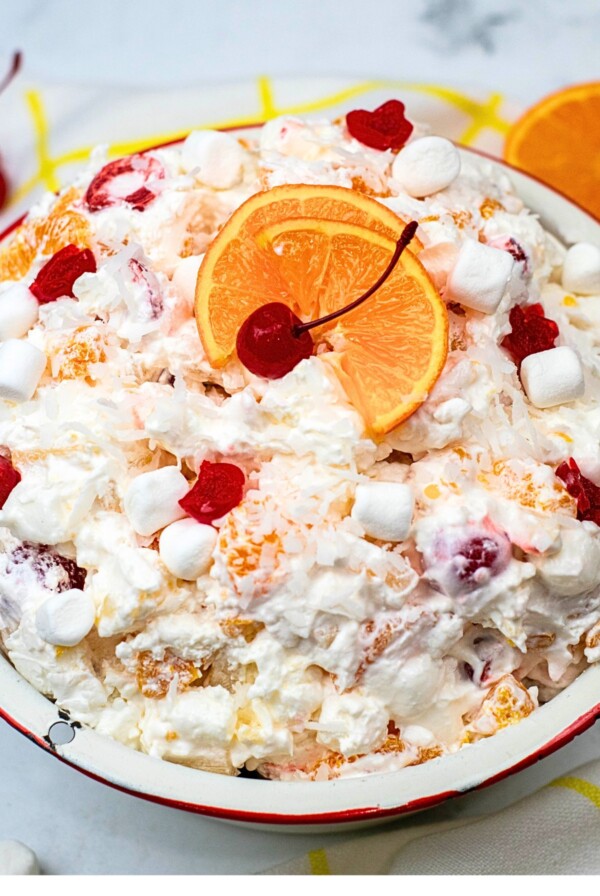 Large bowl filled with ambrosia salad, topped with orange slices and cherries.
