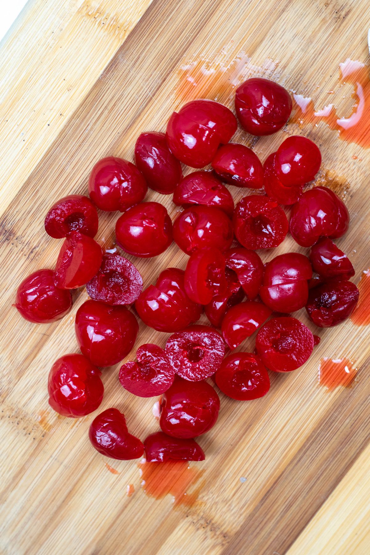 Maraschino cherries on a cutting board, being sliced in half. 