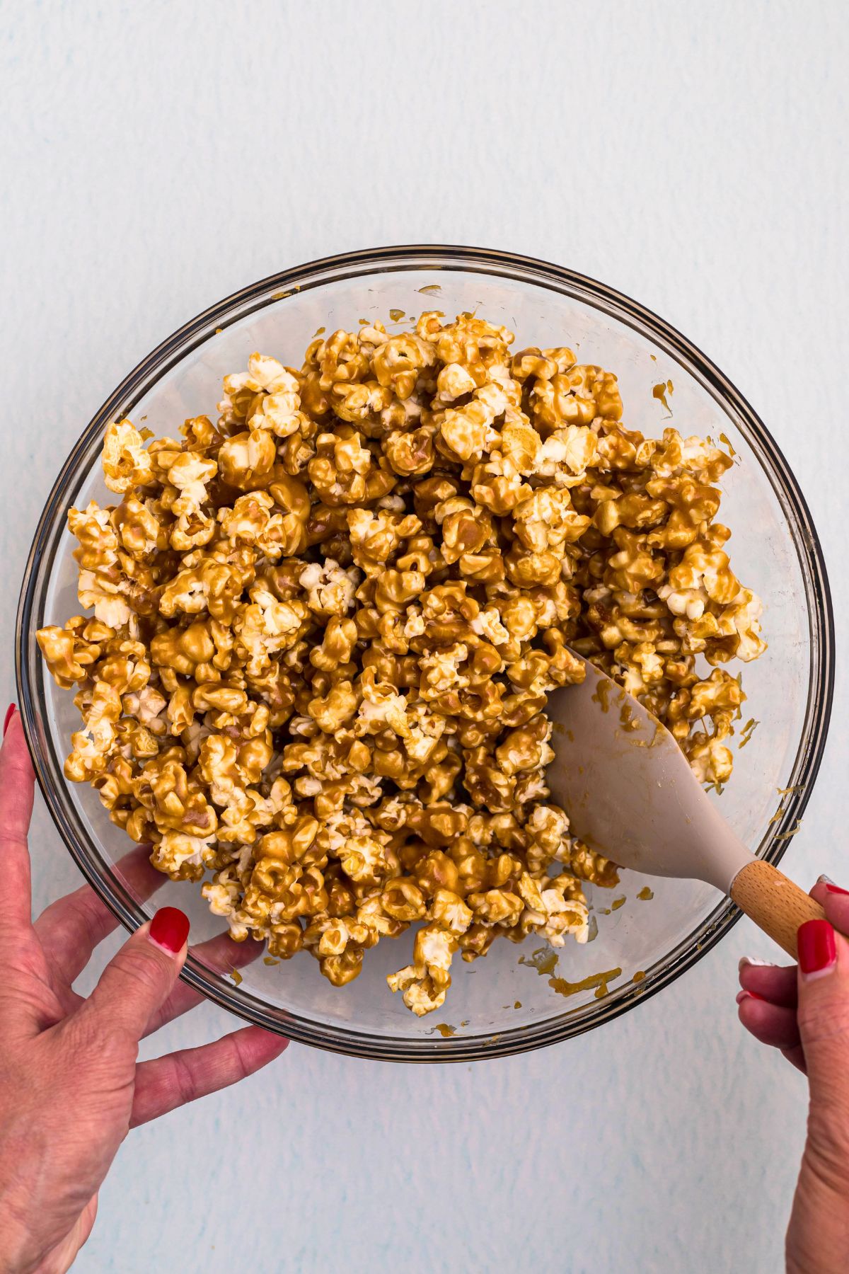 Large clear bowl with caramel popcorn mixed with sauce. 