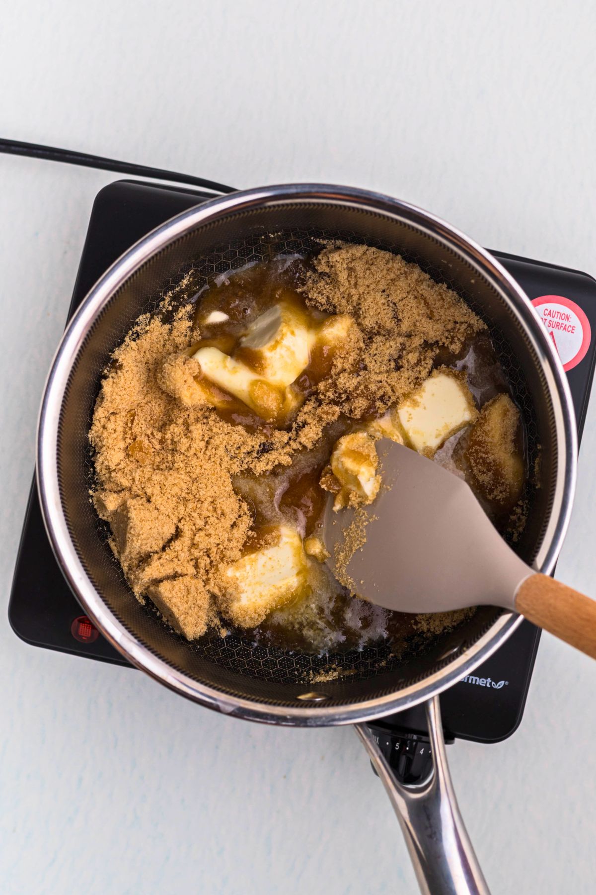 Butter, brown sugar, and other ingredients, being melted and boiled together in a medium saucepan.