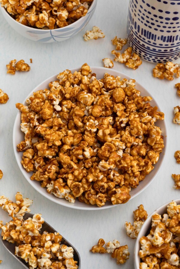 Golden caramel popcorn in a white bowl with pieces of popcorn scattered around the bowl.