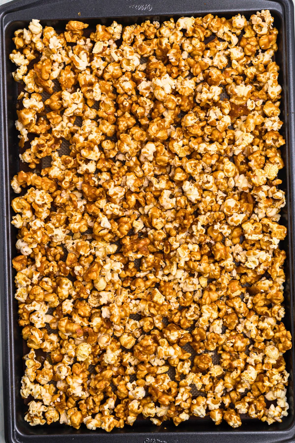 Caramel popcorn spread out in a baking sheet, after baking, showing coated popcorn. 