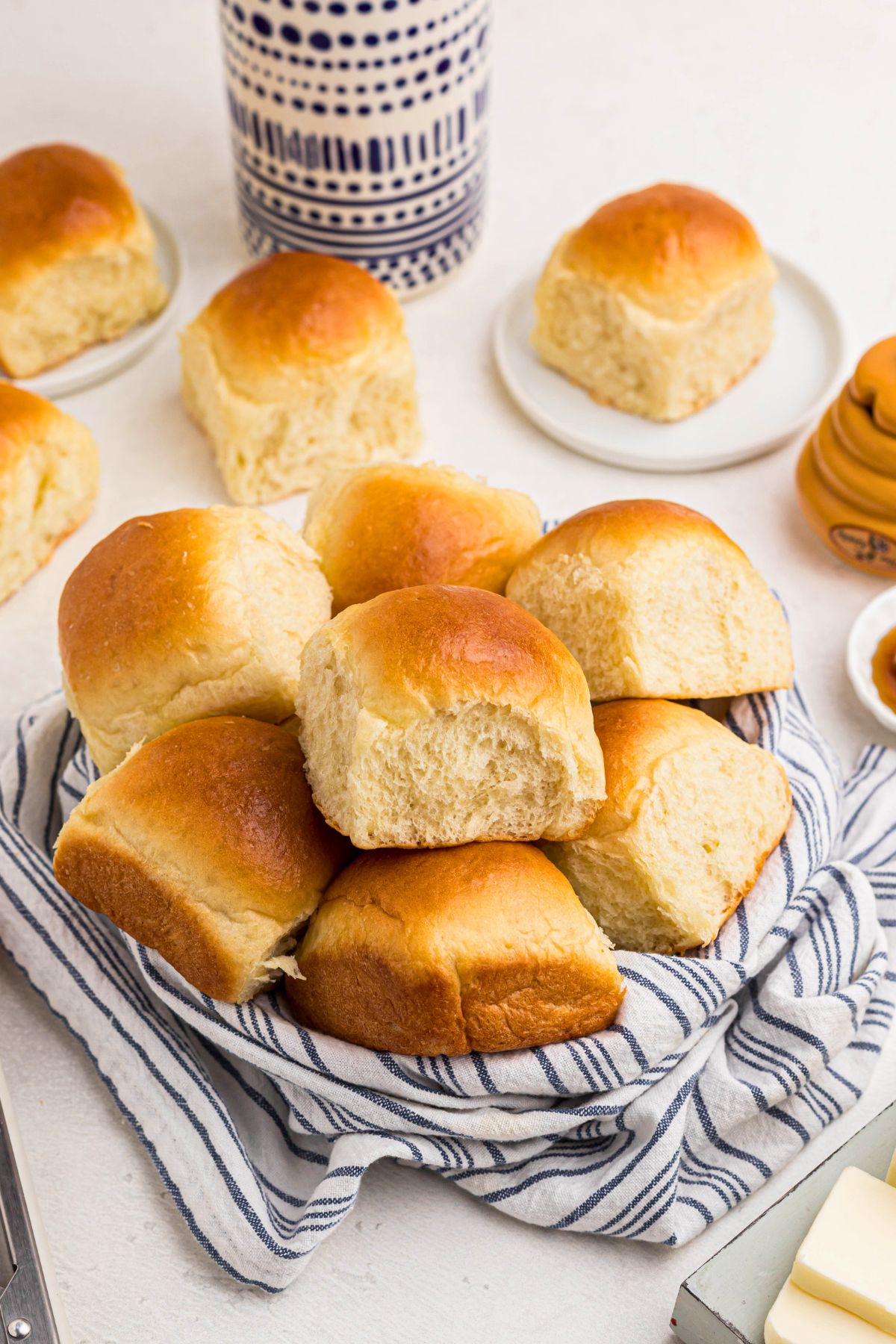 Golden rolls in a small bowl lined with a blue and white linen, on a white marble table. 