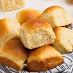 Golden rolls in a small bowl lined with a blue and white linen, on a white marble table.