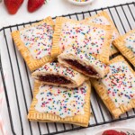 Golden crusted pie crusts, cut into rectangles, filled with strawberry jam, and topped with white icing and sprinkles, on a white rectangle plate.