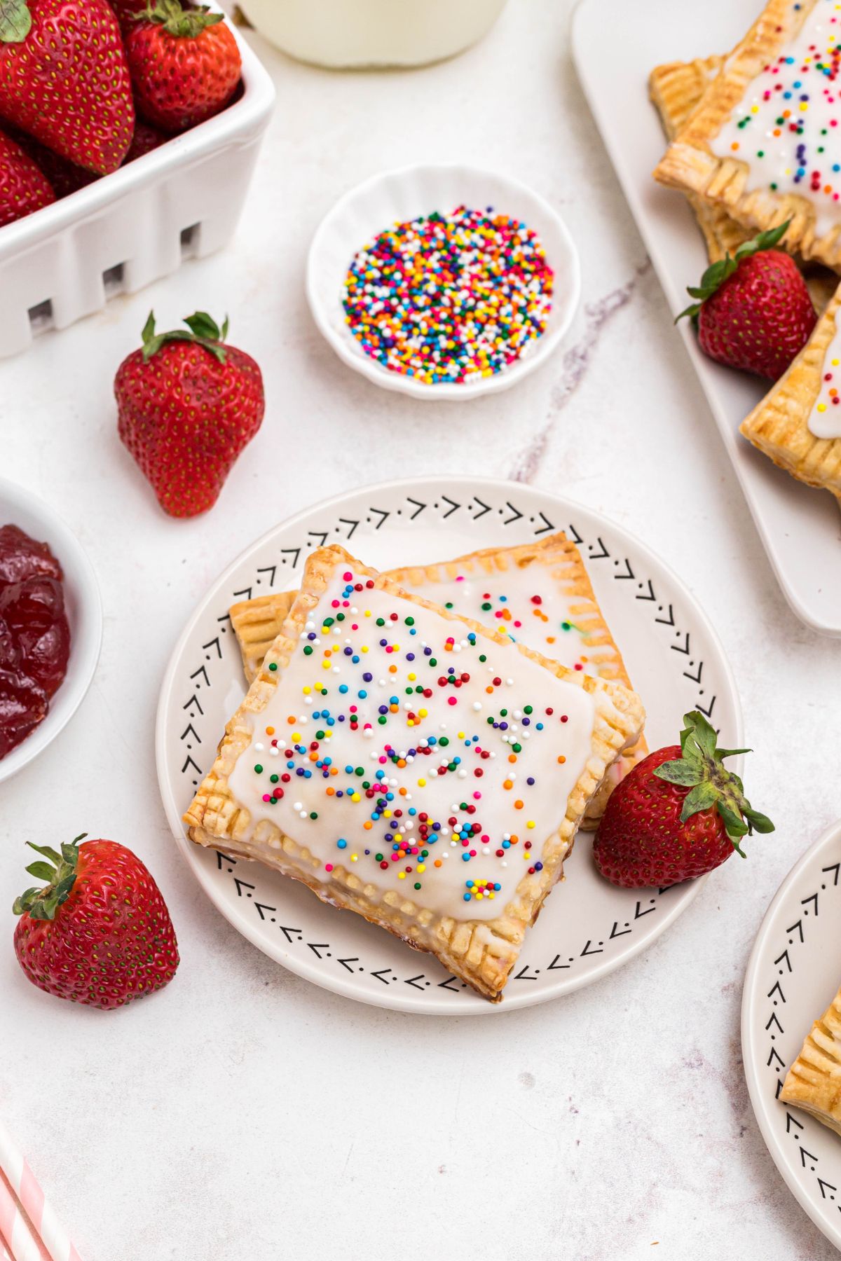 Golden baked stuffed pastries on a small white plate, with fresh strawberries and sprinkles on the table. 