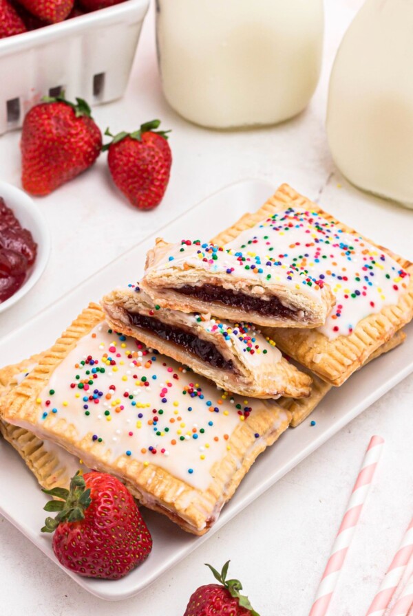 Golden crusted pie crusts, cut into rectangles, filled with strawberry jam, and topped with white icing and sprinkles, on a white rectangle plate.