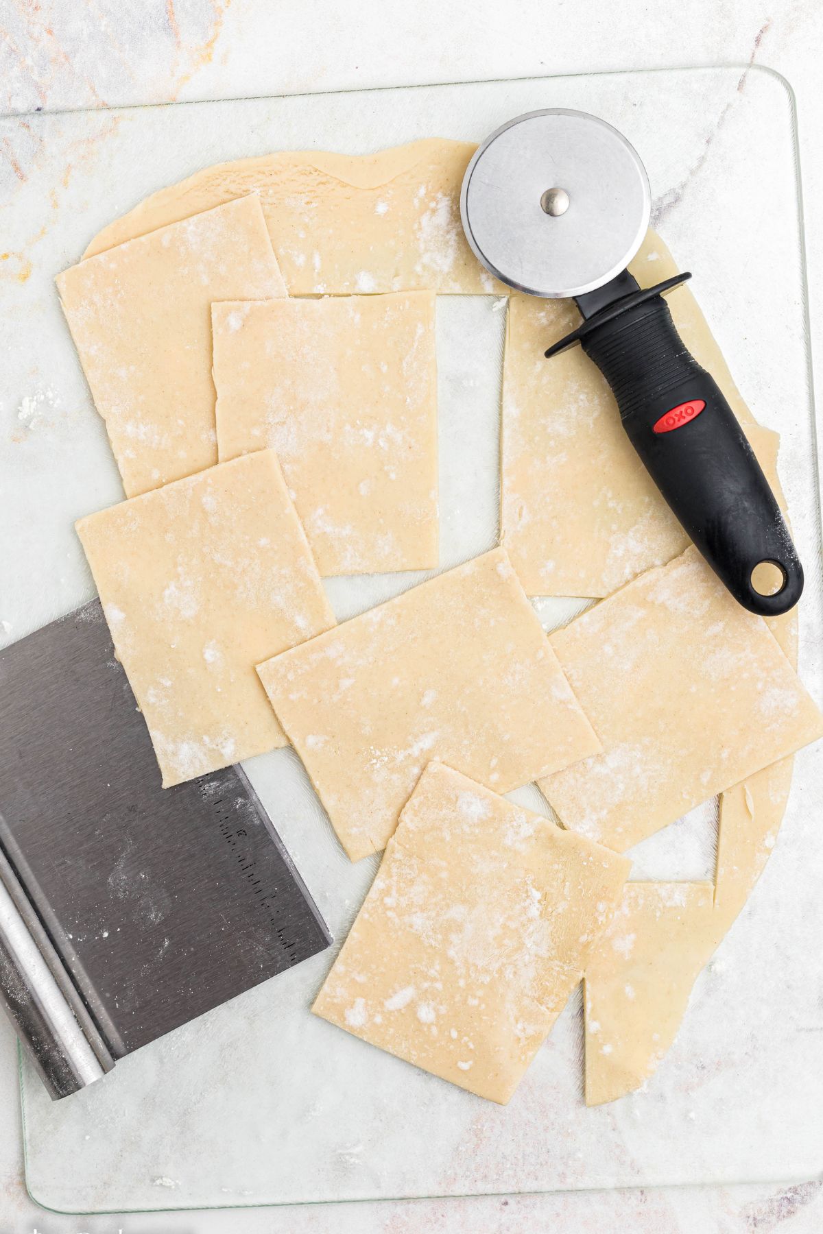 Rolled out pie dough, on a marble table, cut into small squares by a pizza cutter. 