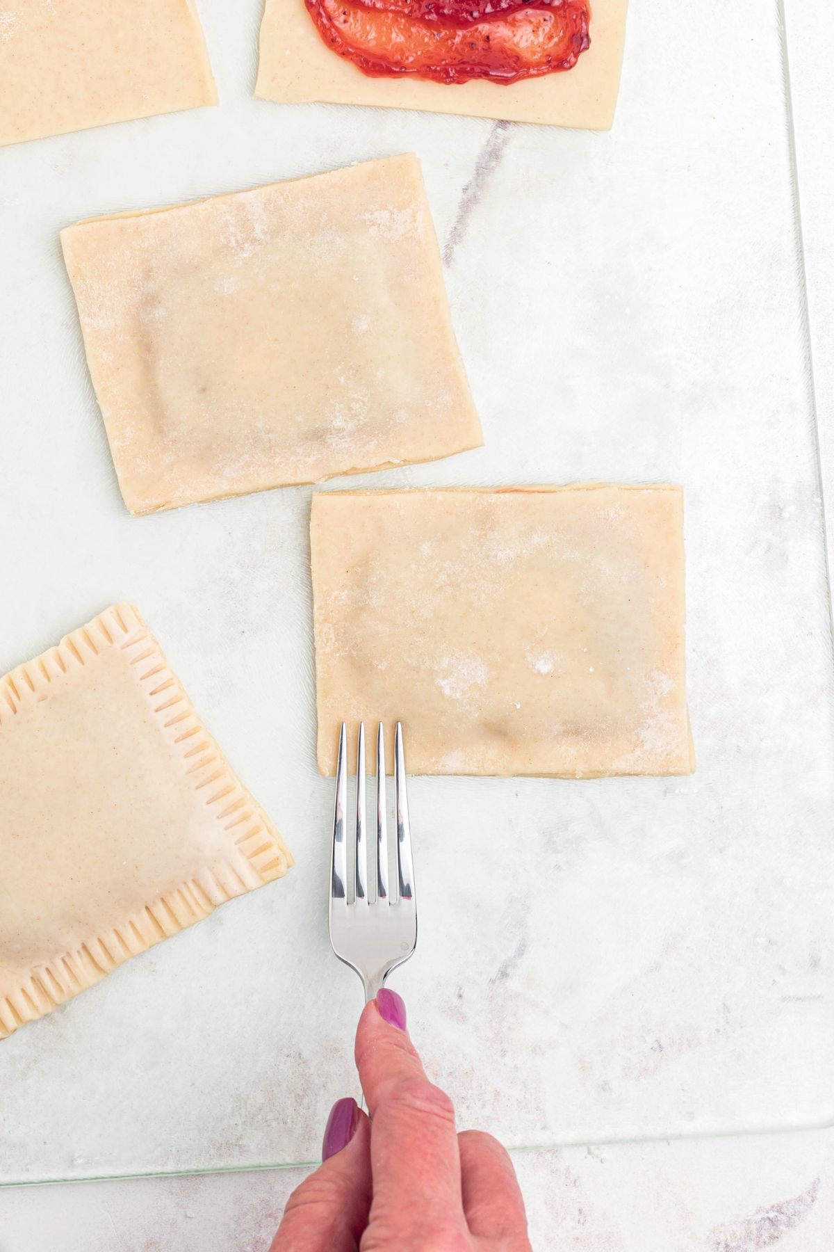 Crusts being filled with jam, and then being sealed with a fork being pressed into the edges. 