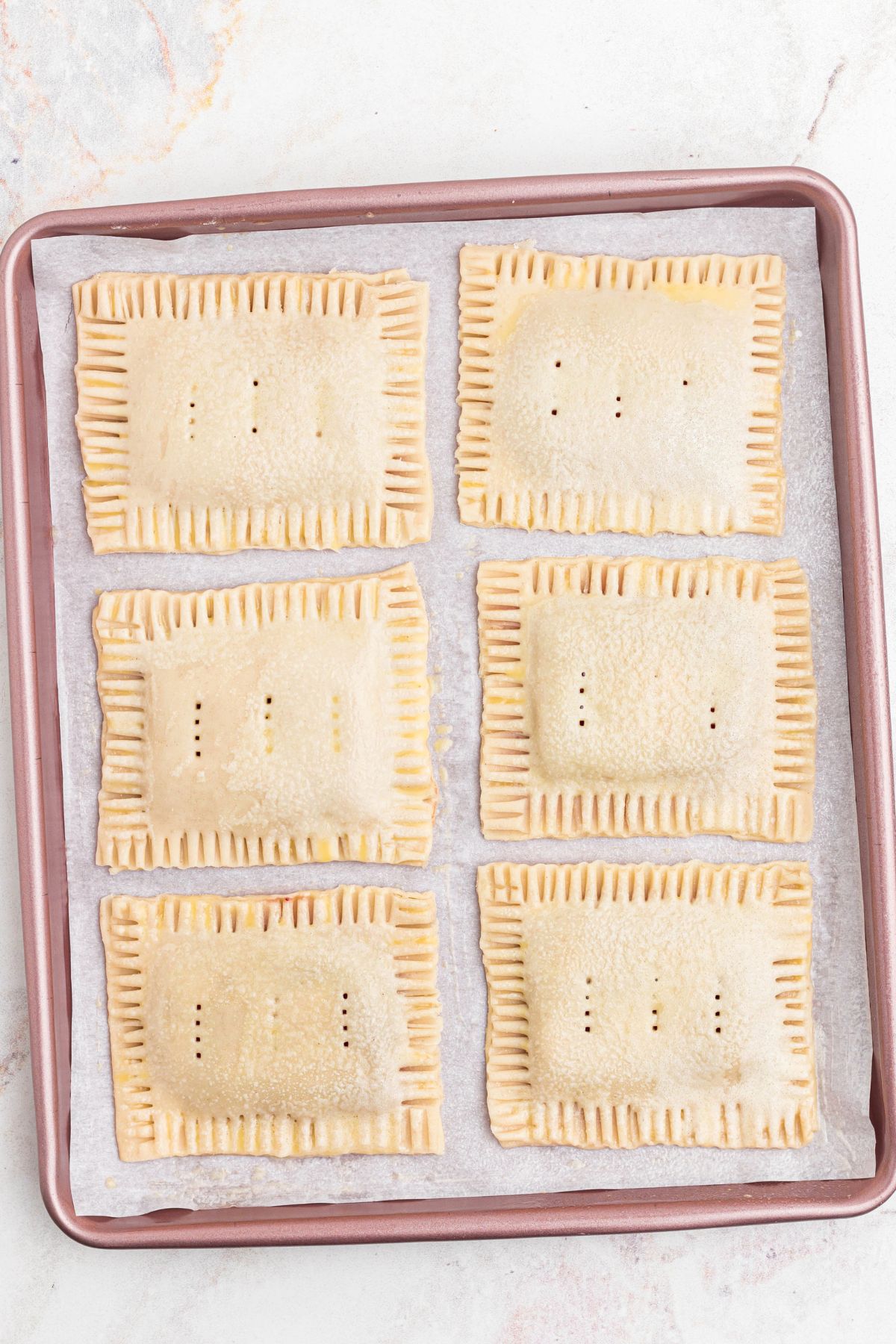 Pastries on a baking sheet, lined with parchment paper, before baking.