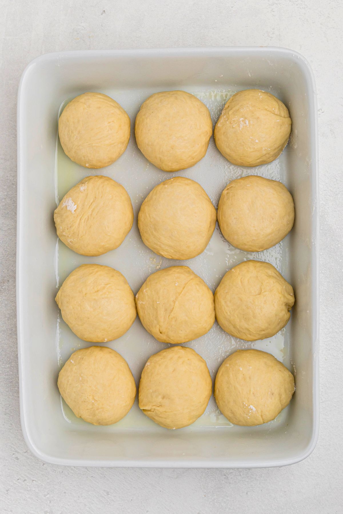 Uncooked roll dough shaped and placed in a white baking dish. 