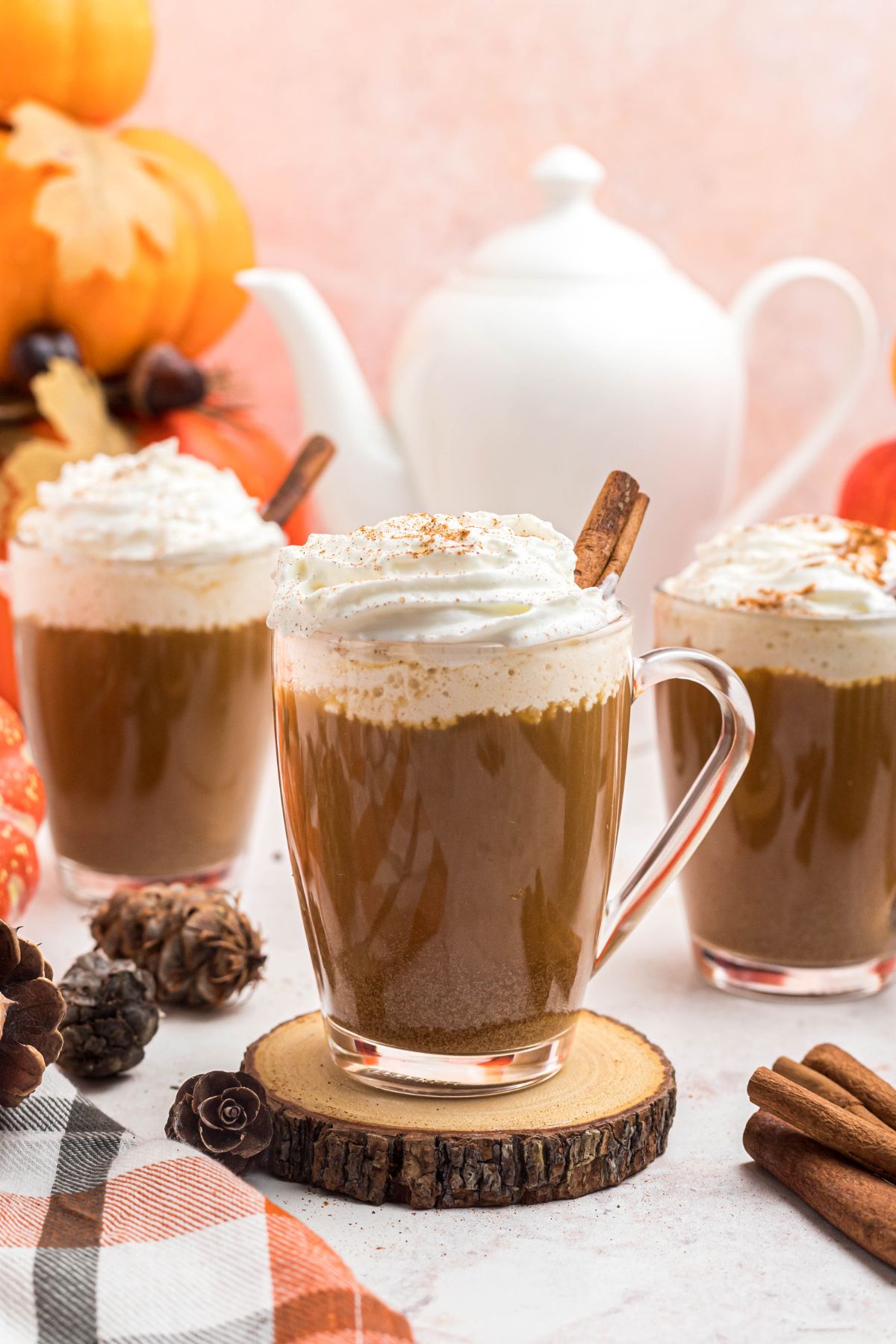 Cups of coffee topped with whipped cream, in front of white pot, on a marble board. 