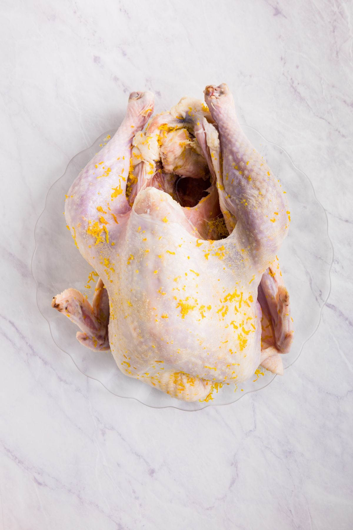 Uncooked chicken rubbed in a brine of seasonings and orange zest, on a marble table. 