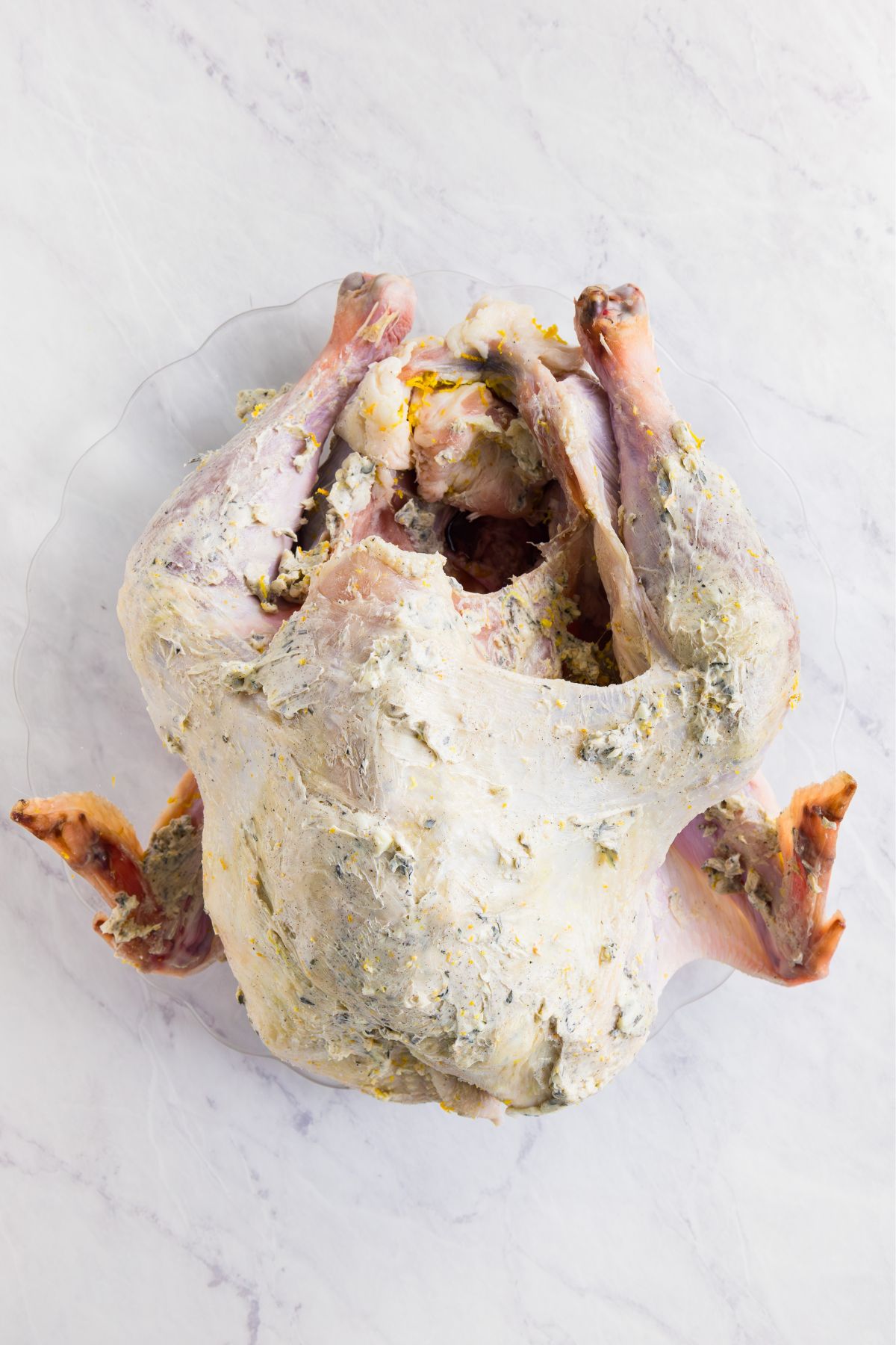 Uncooked turkey on a marble table, covered with a garlic herb butter. 