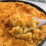 Smoked, cheesy mac and cheese in a black cast iron skillet with a spoon scooping a serving some out.