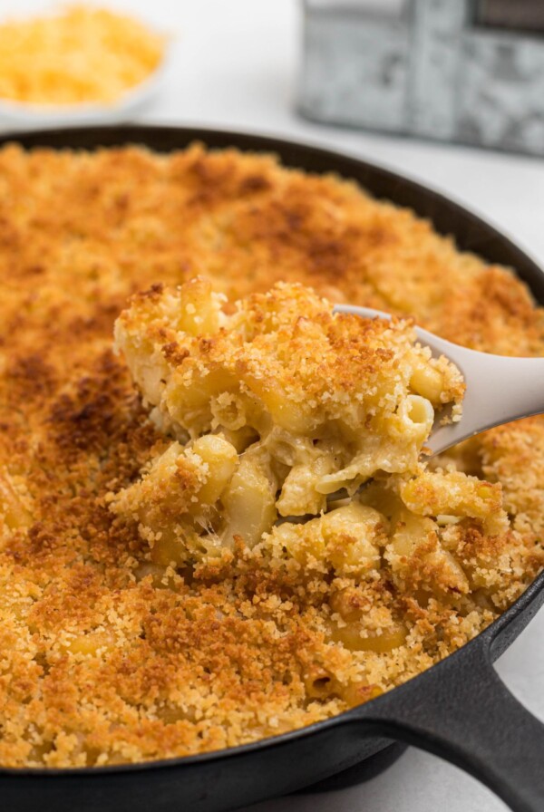 Smoked, cheesy mac and cheese in a black cast iron skillet with a spoon scooping a serving some out.