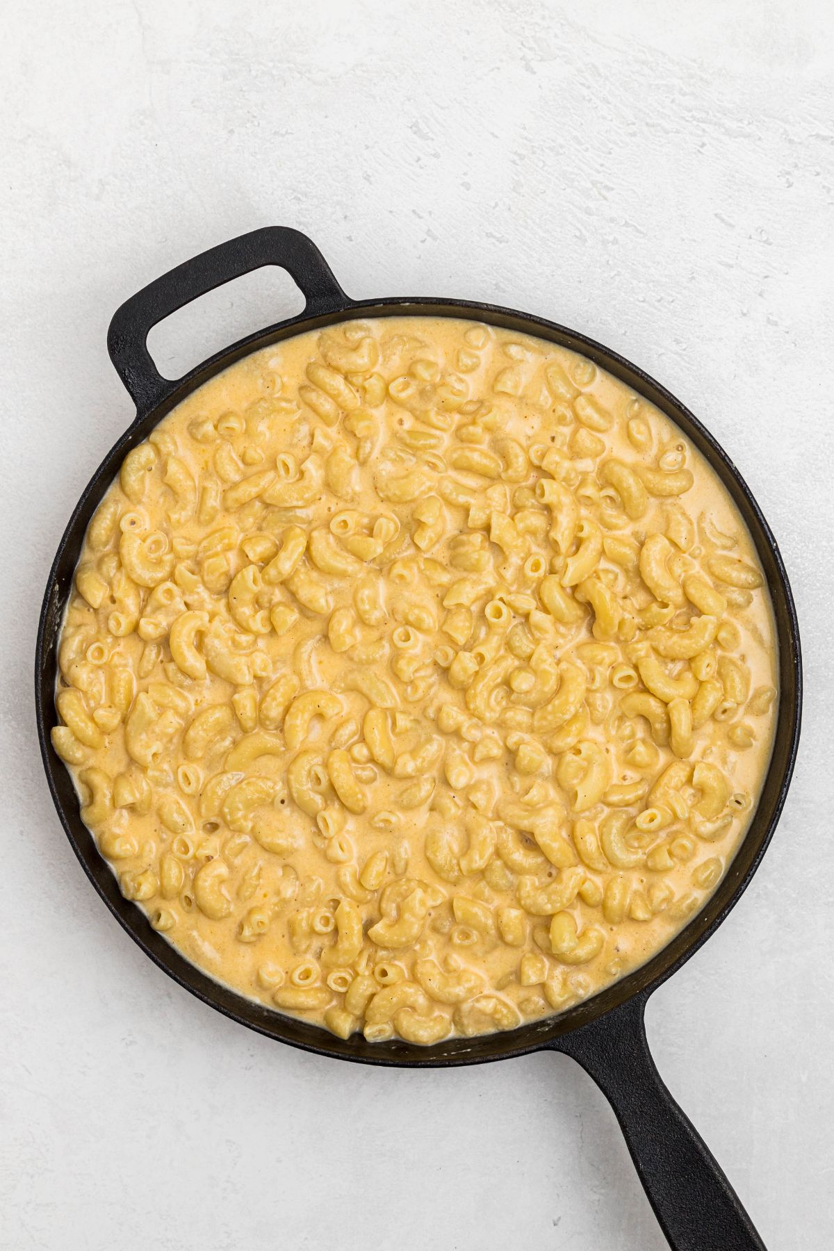 Melted cheese mixture combined with pasta, in a cast iron skillet, on a white marble table. 