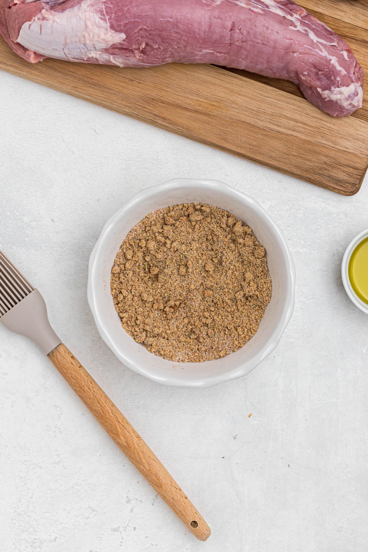 Seasonings and brown sugar in a small white bowl, mixed together, on a white marble table, before being added to the pork tenderloins and smoked. 