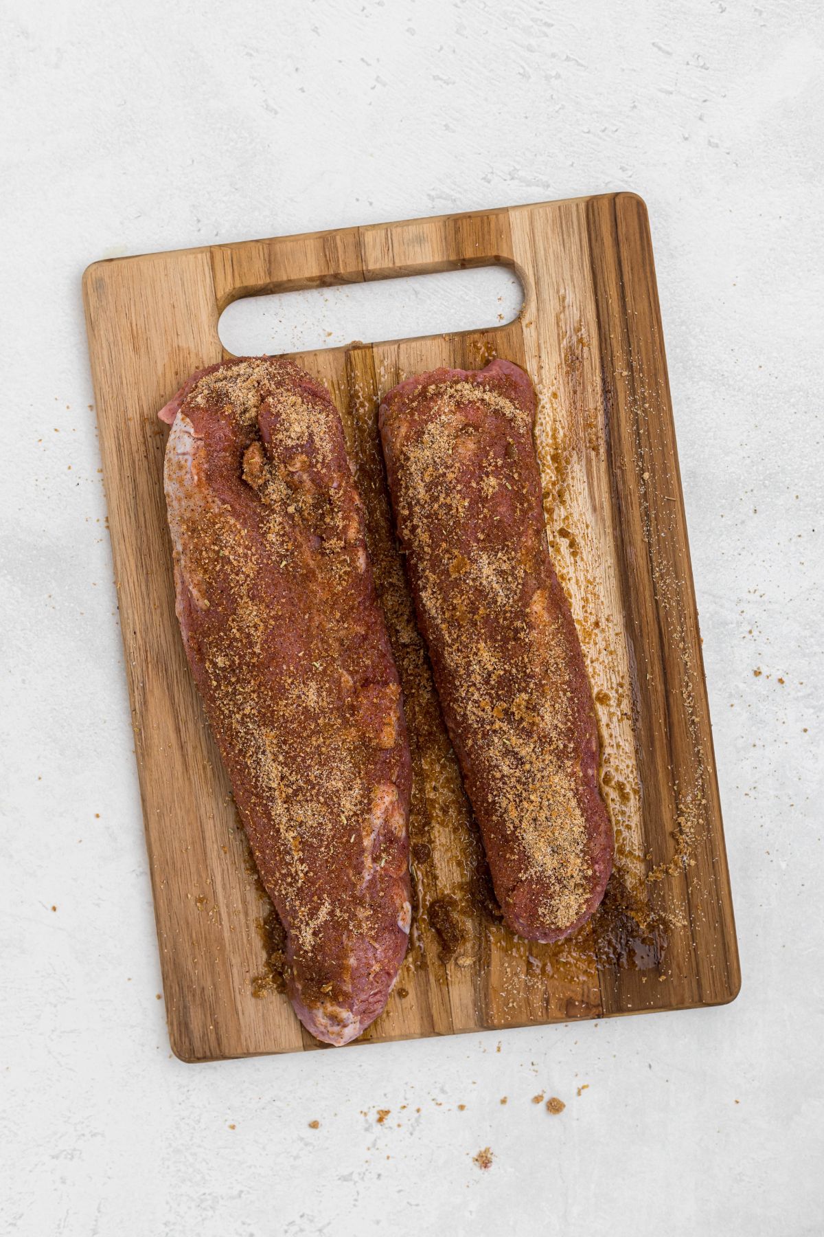 Uncooked, seasoned pork tenderloins on  wooden cutting board. 