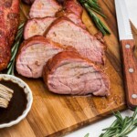 Juicy tenderloin cut into slices on a cutting board with a knife and fork, and fresh rosemary.