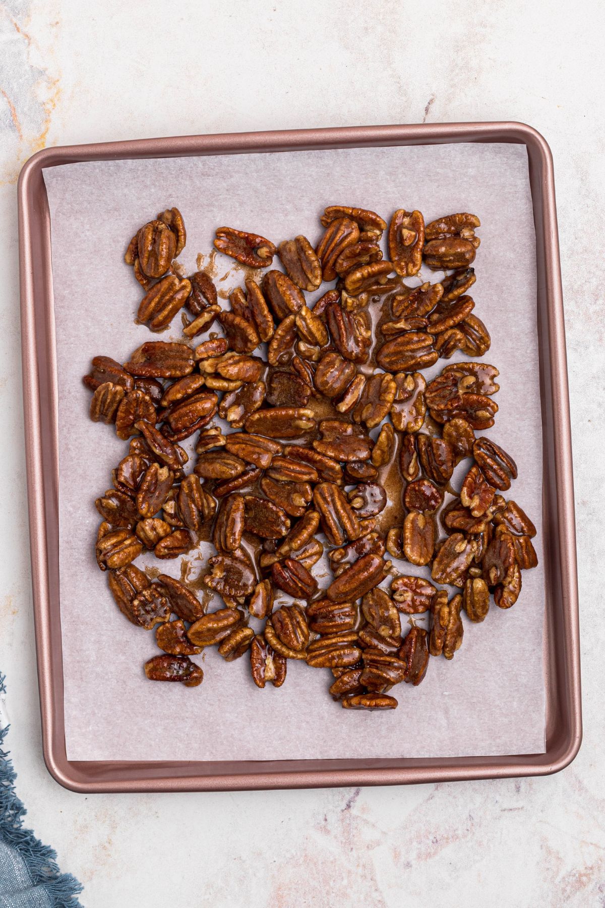 Coated pecans spread onto baking sheet, lined with parchment paper, before baking. 