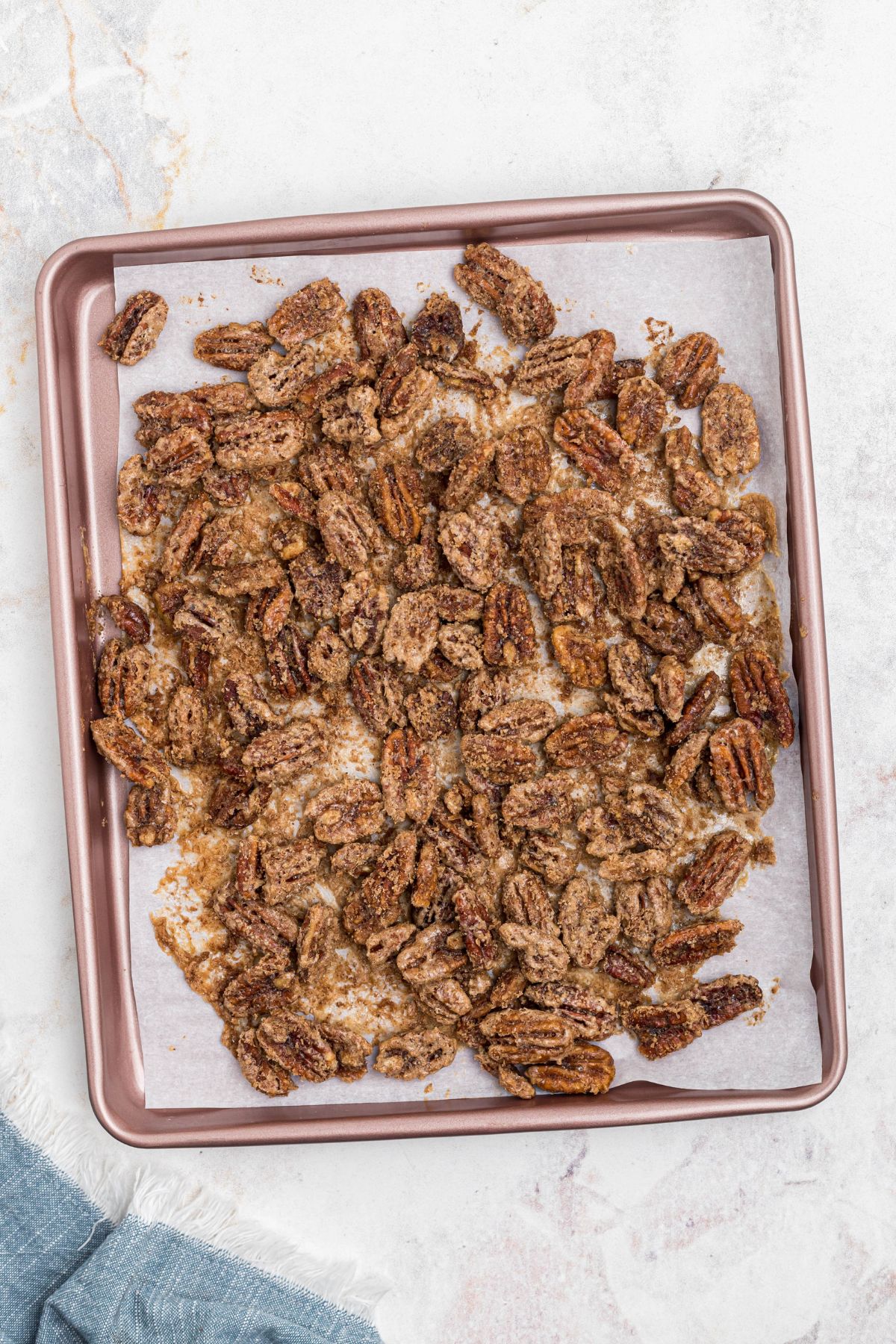Pecans on baking sheet lined with parchment paper, coated with sugar, after baking. 