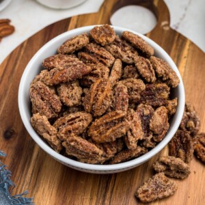 Sugar coated pecans in a white bowl with a small jar of sugar behind the bowl.