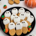 Black plate with peanut butter cookies dipped in white chocolate with chocolate dots for eyes, stacked together, on a marble table.