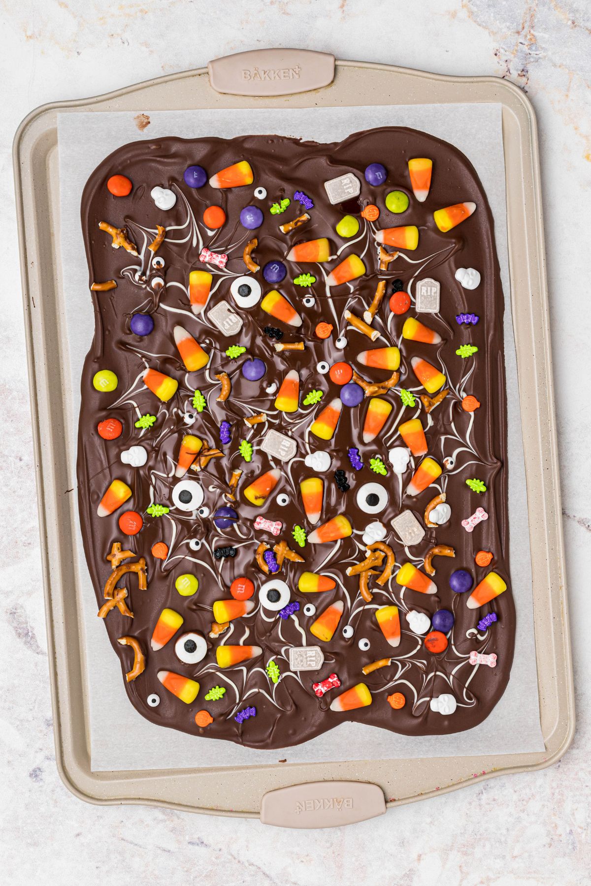 Chilled layer of chocolate, topped with candies and other toppings, in a baking sheet lined with parchment paper. 