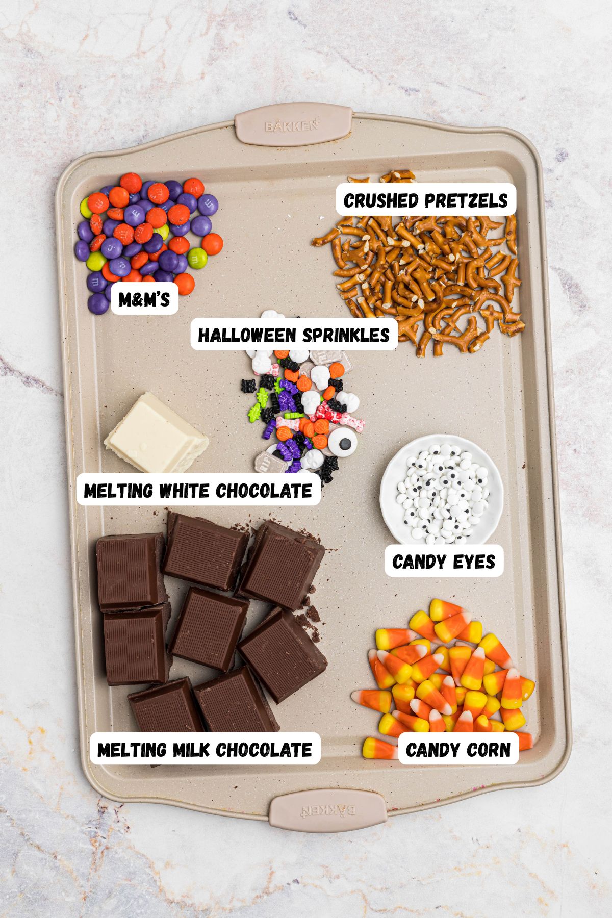 Ingredients needed to make Halloween bark, measured into small bowls, on a baking sheet, and labeled. 