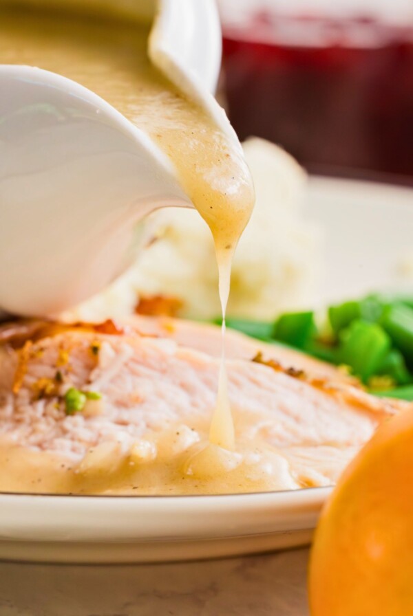 Homemade gravy being poured over slices of turkey, on a white plate.