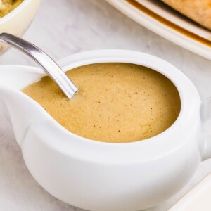 White gravy boat filled with creamy gravy, served with other holiday dishes, on a white marble table.