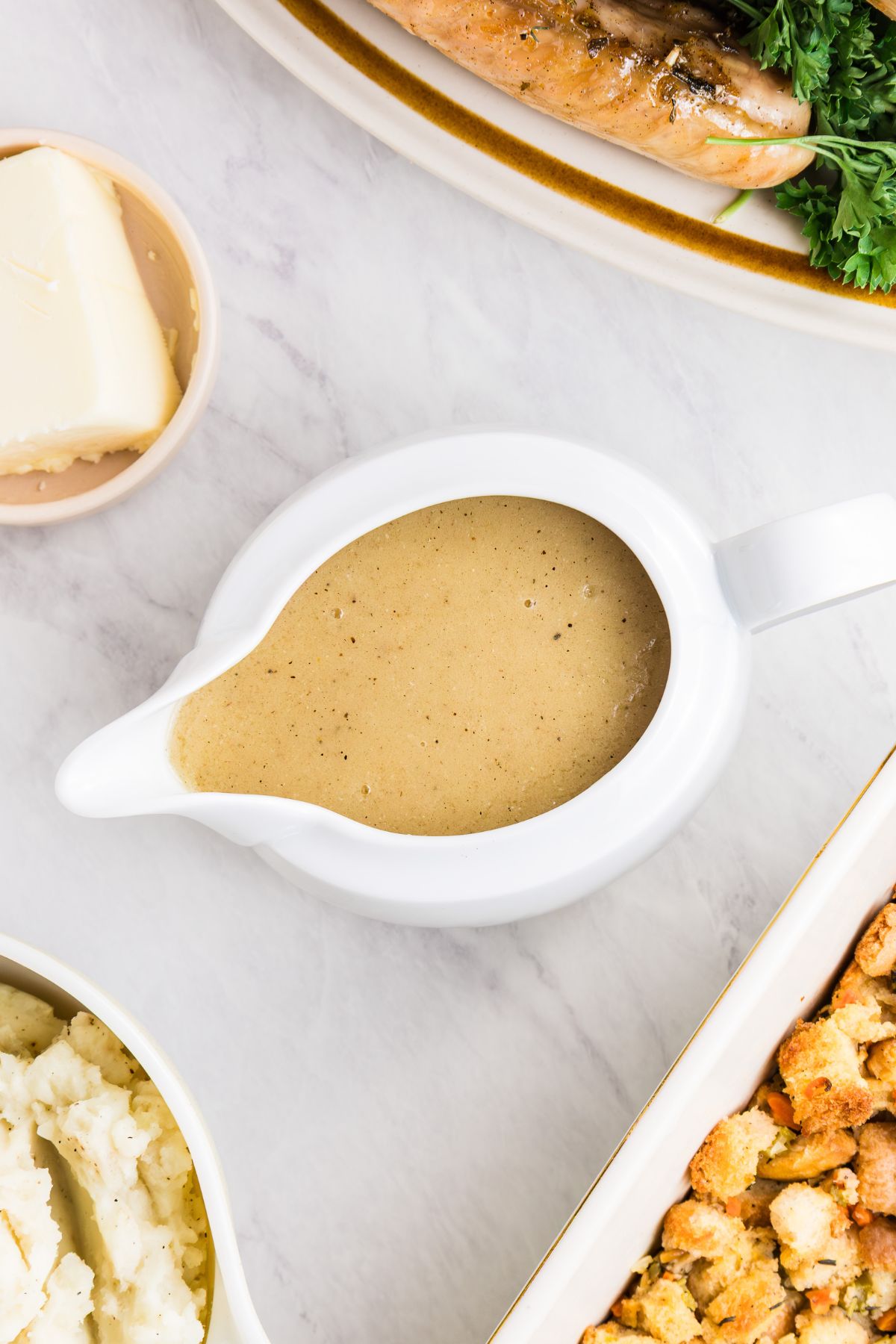 White gravy boat filled with creamy gravy,  served with other holiday dishes, on a white marble table.