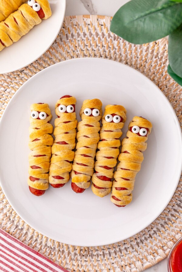 Mummy hot dogs on a white plate, with candy eyes.