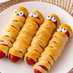 Mummy hot dogs on a white plate, with candy eyes.