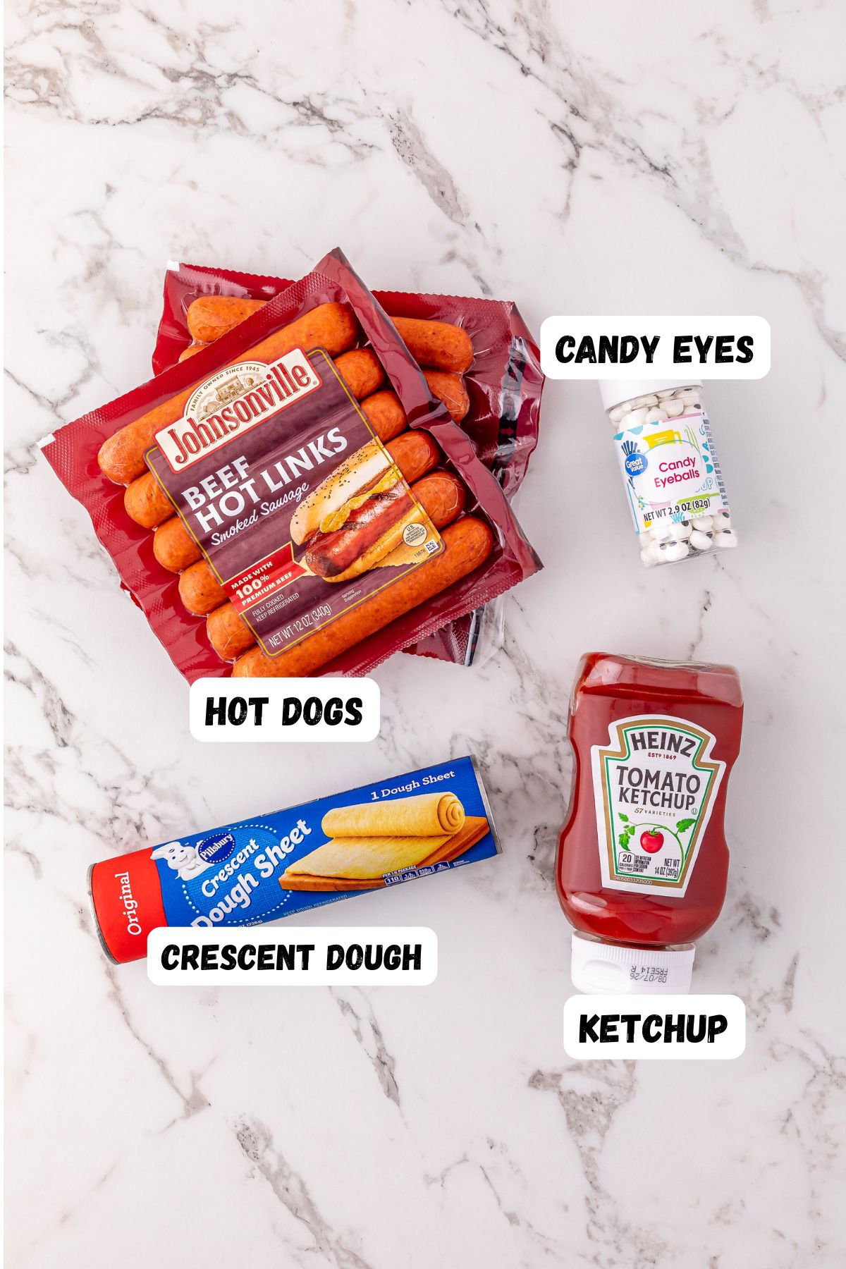 Ingredients needed to make Mummy Hot Dogs on a marble table and labeled.