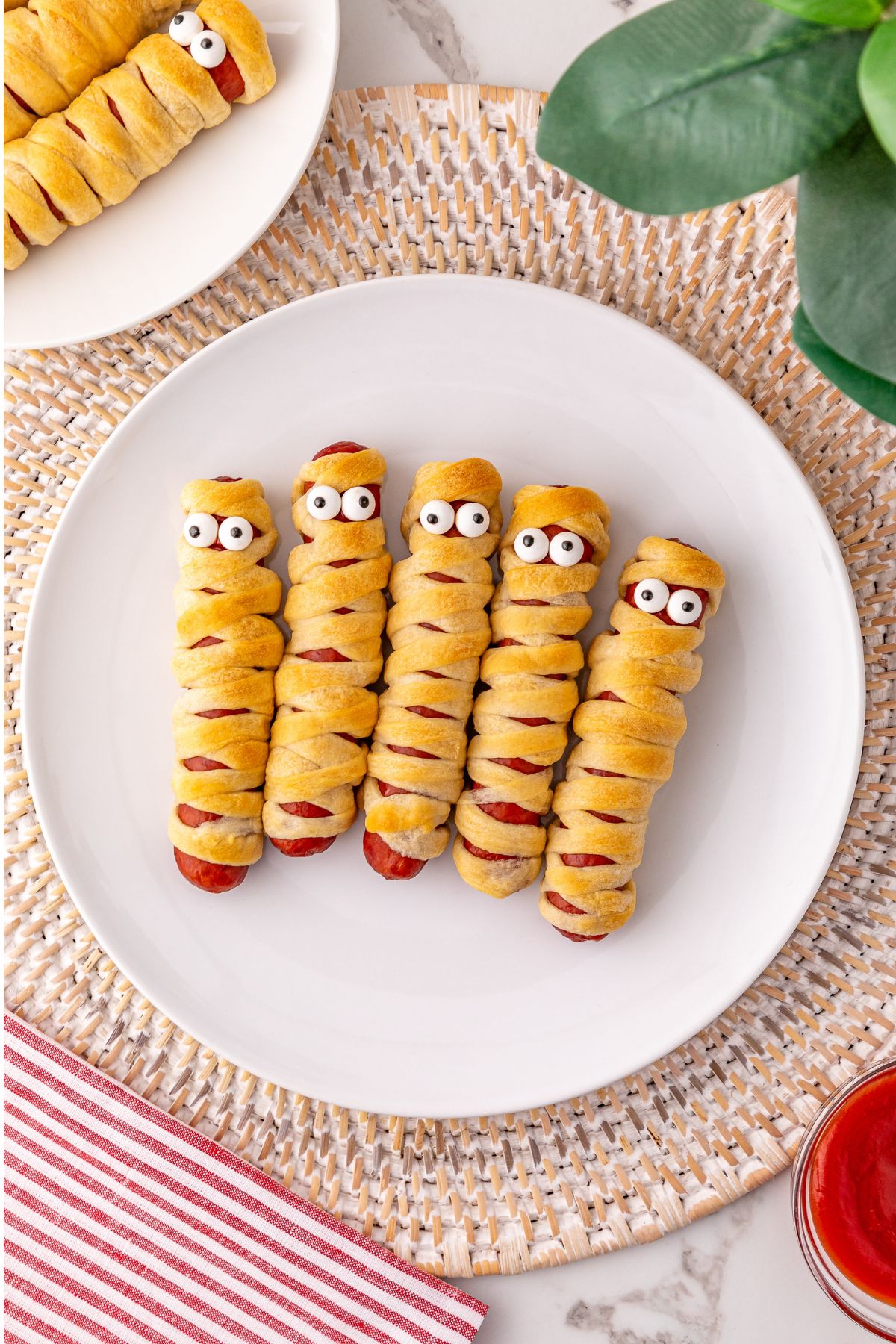 Mummy hot dogs on a white plate, with candy eyes.